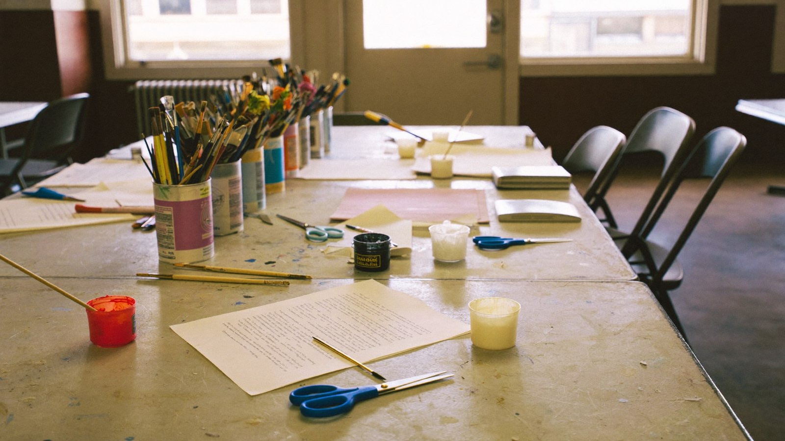 A community hall craft table mid-project, with paint pots, brushes and half-finished work spread across it.