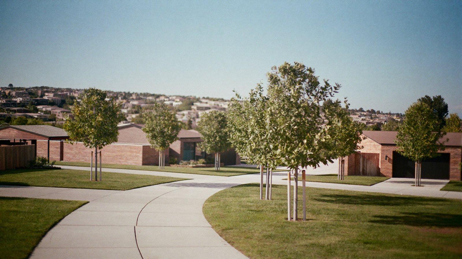 A wide new concrete footpath curving between lawns and young street trees, past low brick homes in a new Western Sydney suburb.