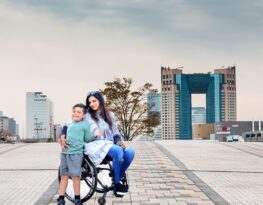 Woman is sitting on chair wheel while taking a picture with child